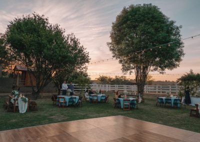 Backyard wedding in Queen Creek AZ decorated with round tables, fruitwood chairs, a dance floor, and custom string lighting.