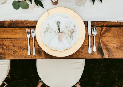 A birds-eye view of a table setting containing a gold charger, candles, and a wood cross back chair with a white cushion