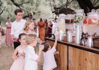 Drink dispensers on a wood bar with children reaching for cups