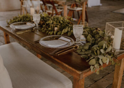 Two place settings at a sweetheart table. The table is decorated with greenery and votive candles