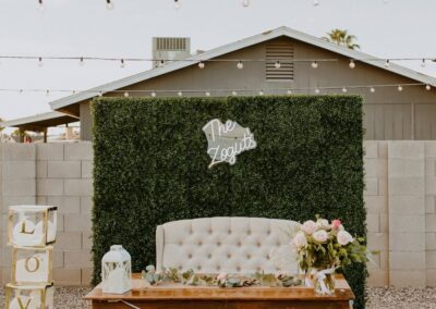 Sweetheart table placed in front of a greenery wall and a loveseat.