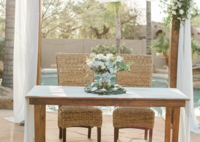 sweetheart table with floral arrangement and banana leaf accent chairs in front of an arch