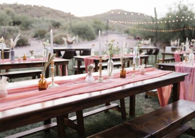 wood table decorated with a pink table runner and various glass vases with flroal stems