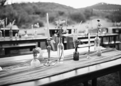 black and white photo of wood table decorated with a pink table runner and various glass vases with flroal stems