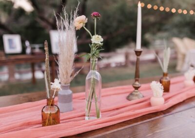 wood table decorated with a pink table runner and various glass vases with flroal stems