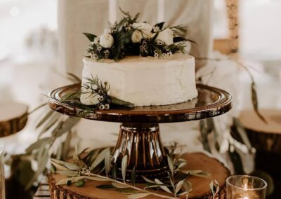 small white cake on a cake stand layered on a wood slice and a wood crate