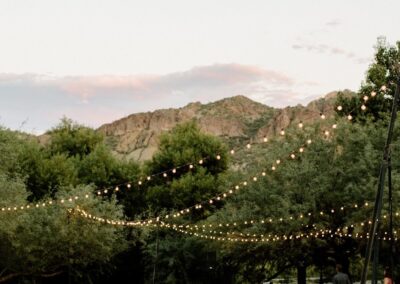 long tables set up around a dance floor with lights strung above at an outdoor wedding venue
