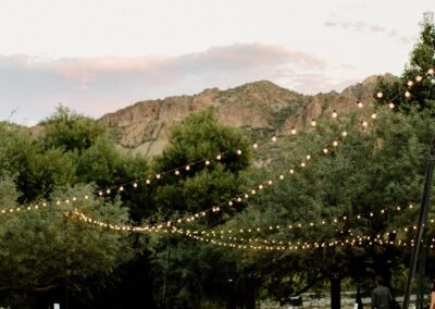 long tables set up around a dance floor with lights strung above at an outdoor wedding venue