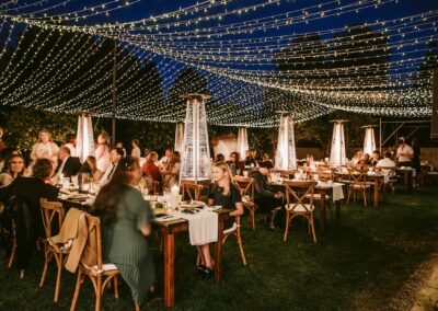 guests sitting at wood tables underneath an outdoor twinkle light canopy
