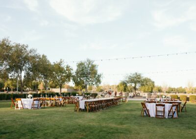 Wood tables and chairs at an outdoor wedding with string lights strung up