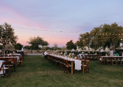 Wood tables and chairs at an outdoor wedding with string lights strung up at sunset