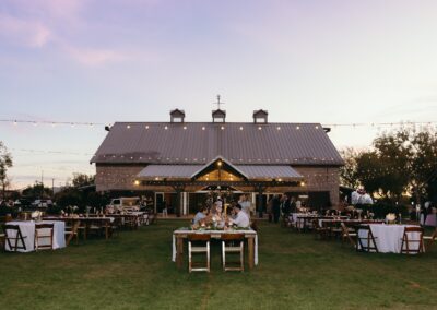 Wood tables and chairs at an outdoor wedding with string lights strung up at sunset