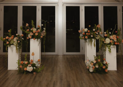 Floral pieces set atop four white columns at an indoor wedding