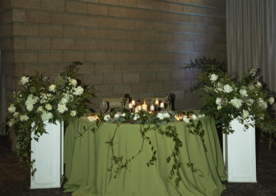 Two white plant stands topped with large floral arrangements framing a sweetheart table at an arizona wedding