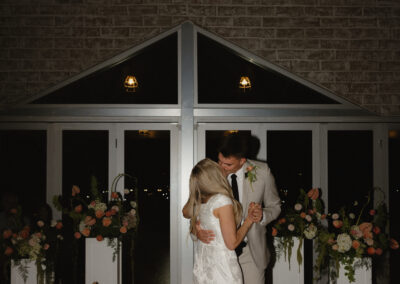 Bride and groom dancing in front of floral arrangements standing on white plant stands at indoor arizona wedding venue